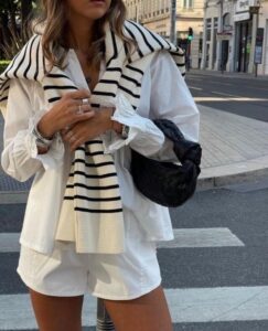 Mulher com look branco e suéter listrado nos ombros, exemplo de old money aesthetic.